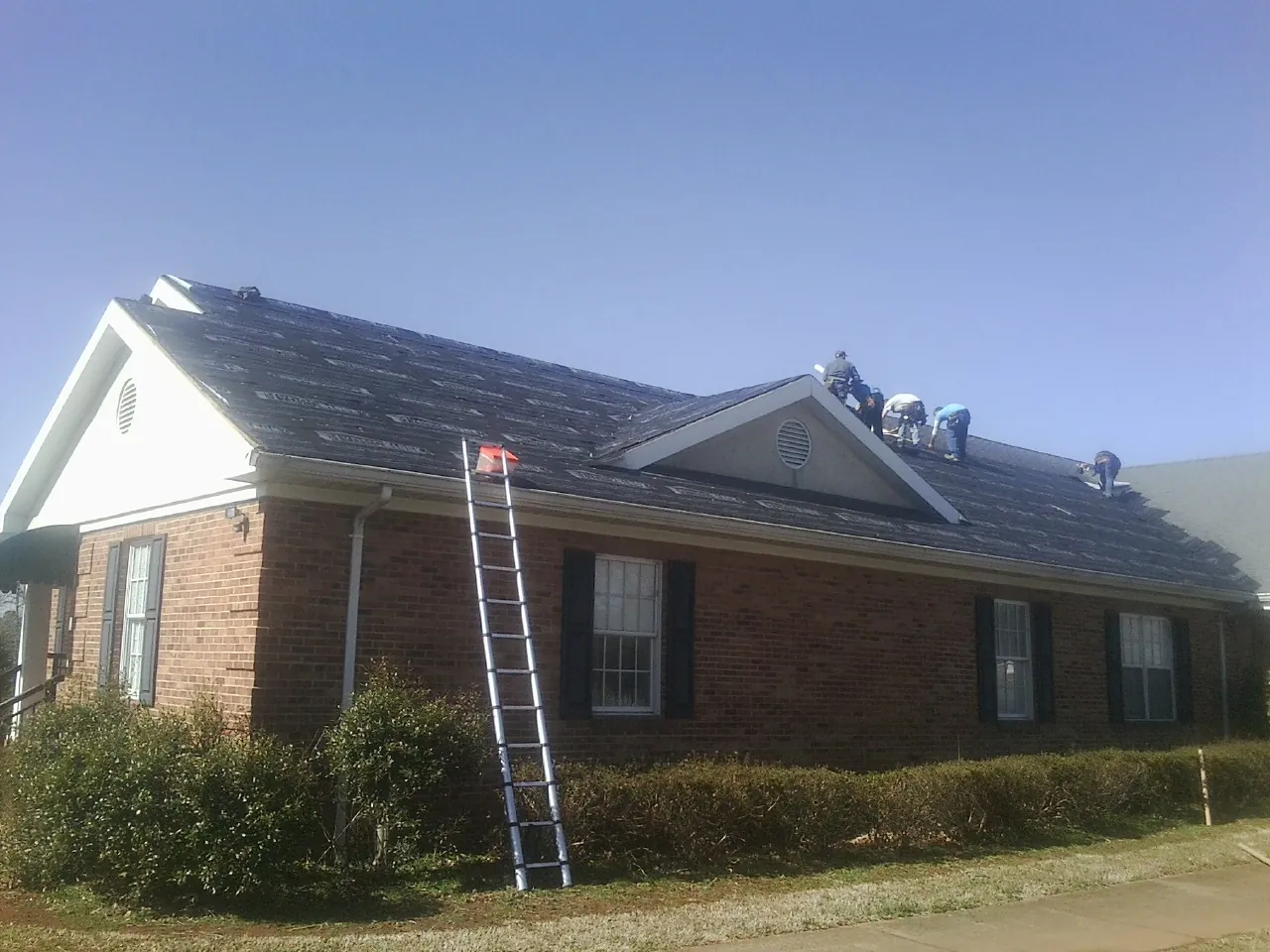 Crew tearing shingles off a brick ranch roof with a ladder set — Metal Roof Repair work by our crew in Brockway