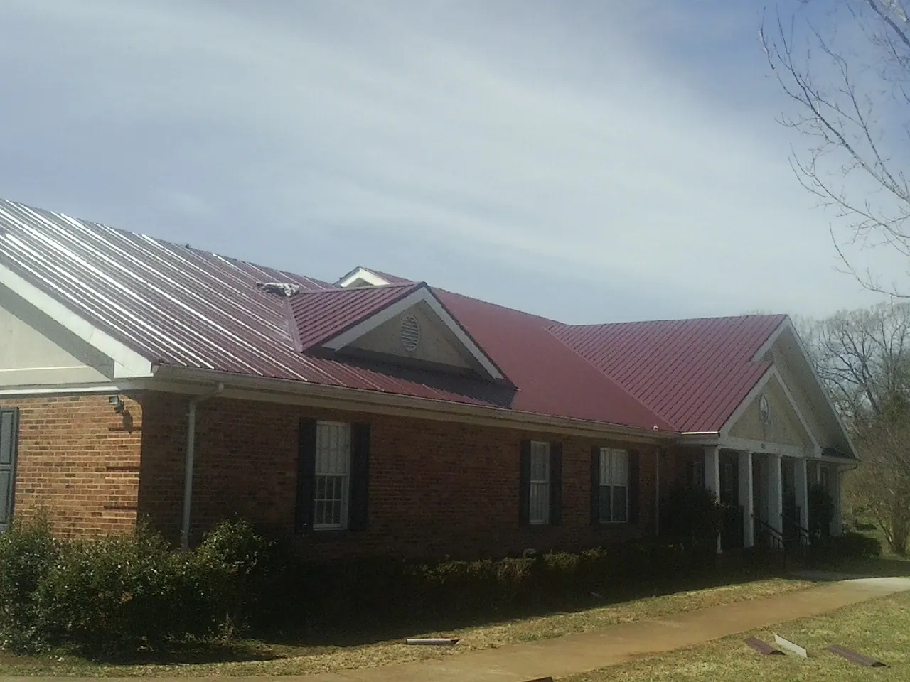 Red metal roof with gabled entries on a long brick building, from a Hail Damage Roof Repair job in Brockway