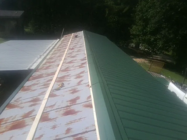 Old rusted panels beside newly installed green metal roofing — Wind Damage Roof Repair by Roofing Brothers in Brockway