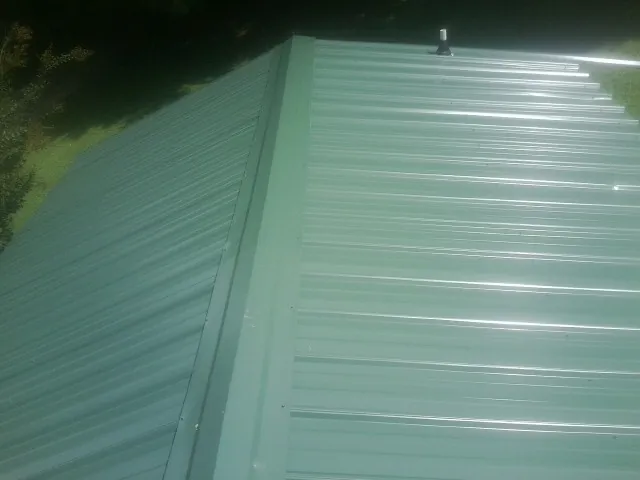 New green metal panels meeting at the ridge of a roof — Flat Roof Repair work by our crew in Brockway