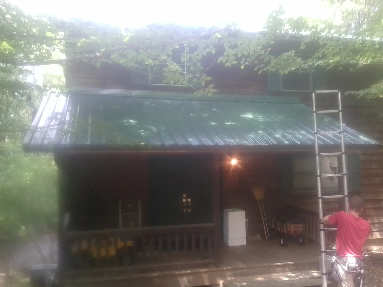 Worker on a ladder at the green porch roof of a wooded cabin in Brockway