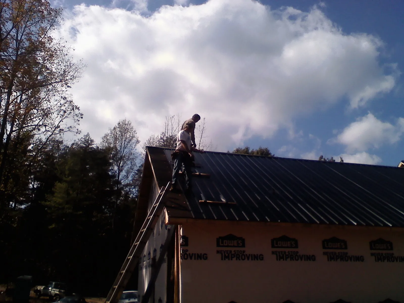 Roofer fastening dark metal panels high against a cloudy sky, from a Roof Inspection job in Brockway