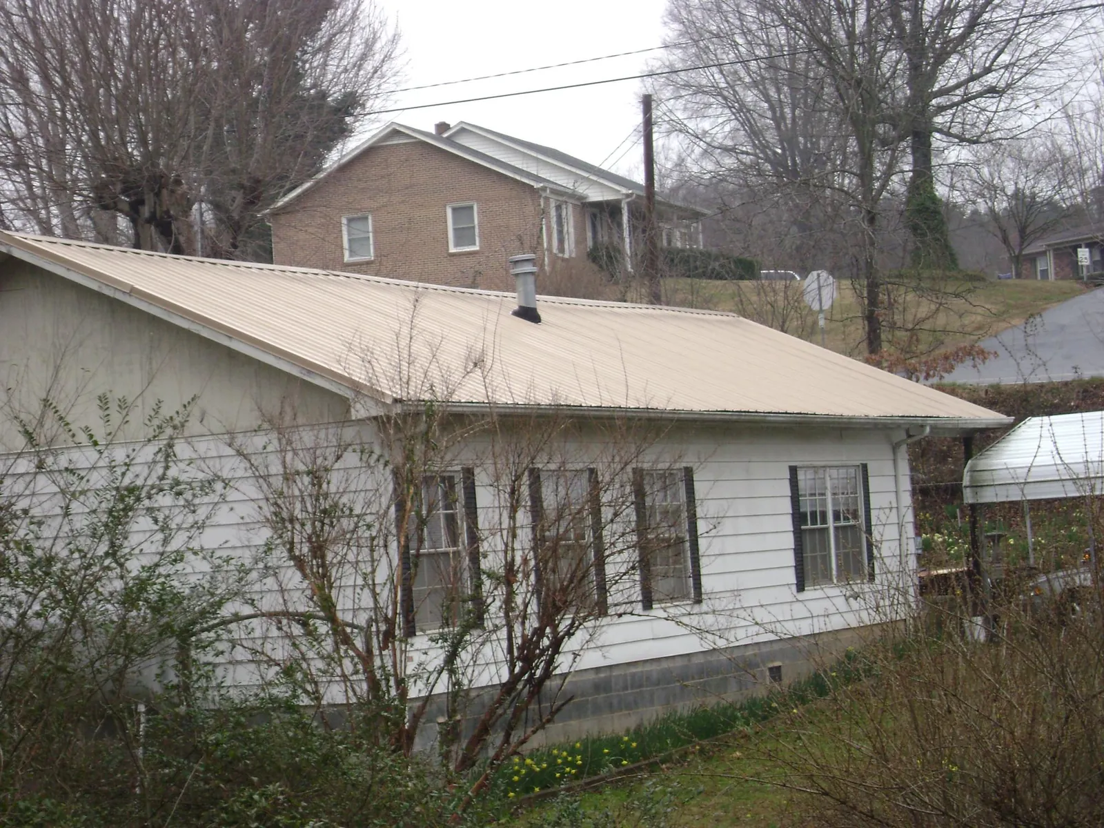 Tan metal roof on a white sided house set into a hillside — Commercial Roofing by Roofing Brothers in Brockway