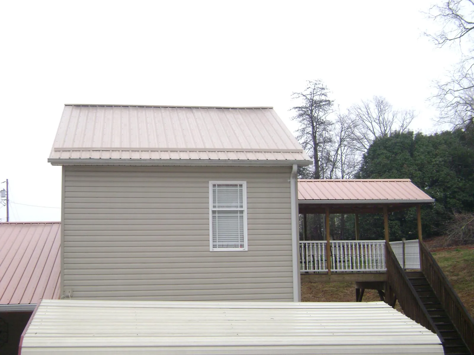 Tan metal roofs on a two story addition and attached porch, from a Roof Replacement job in Brockway